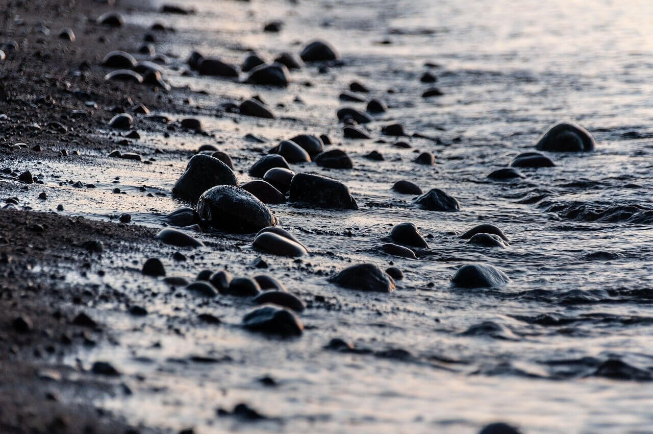 Small rocks are seen in the surf zone of a Lake Superior beach in the fading sunlight.